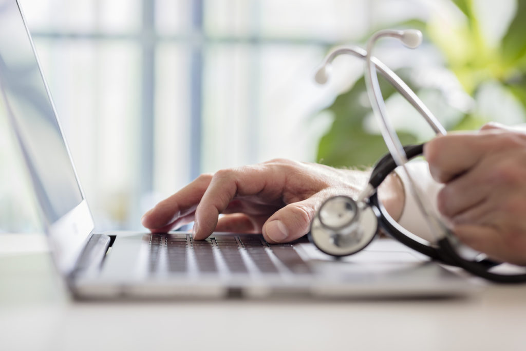 doctor in hospital holding medical device while on laptop