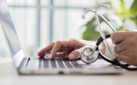 doctor in hospital holding medical device while on laptop